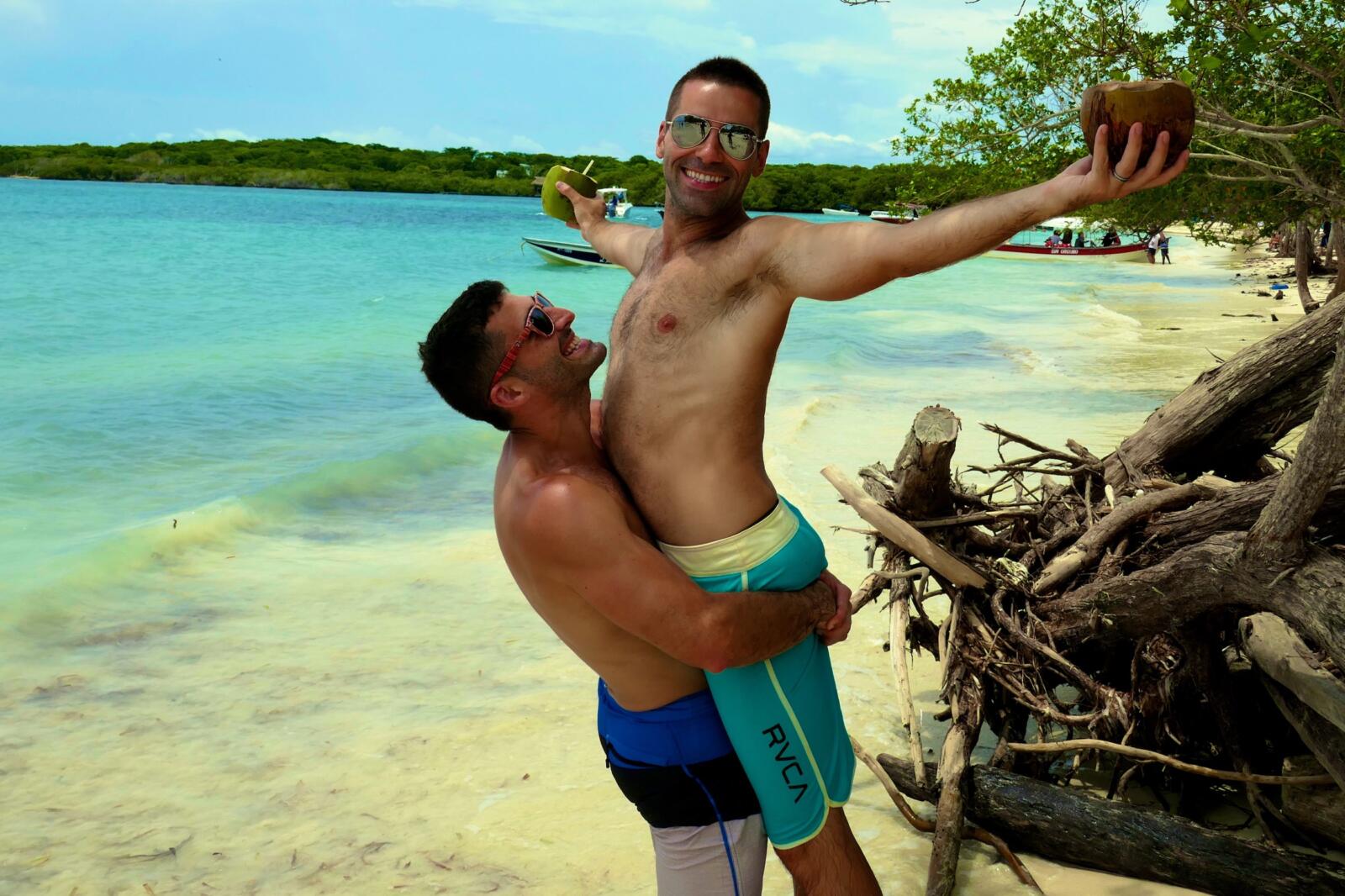 Gay couple embracing with coconuts in hand in the Rosario islands in Cartagena.