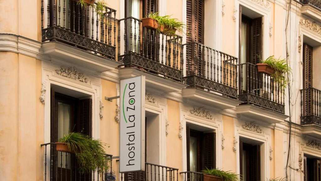 An old building in Madrid with balconies and plants and a sign saying Hostal La Zona.