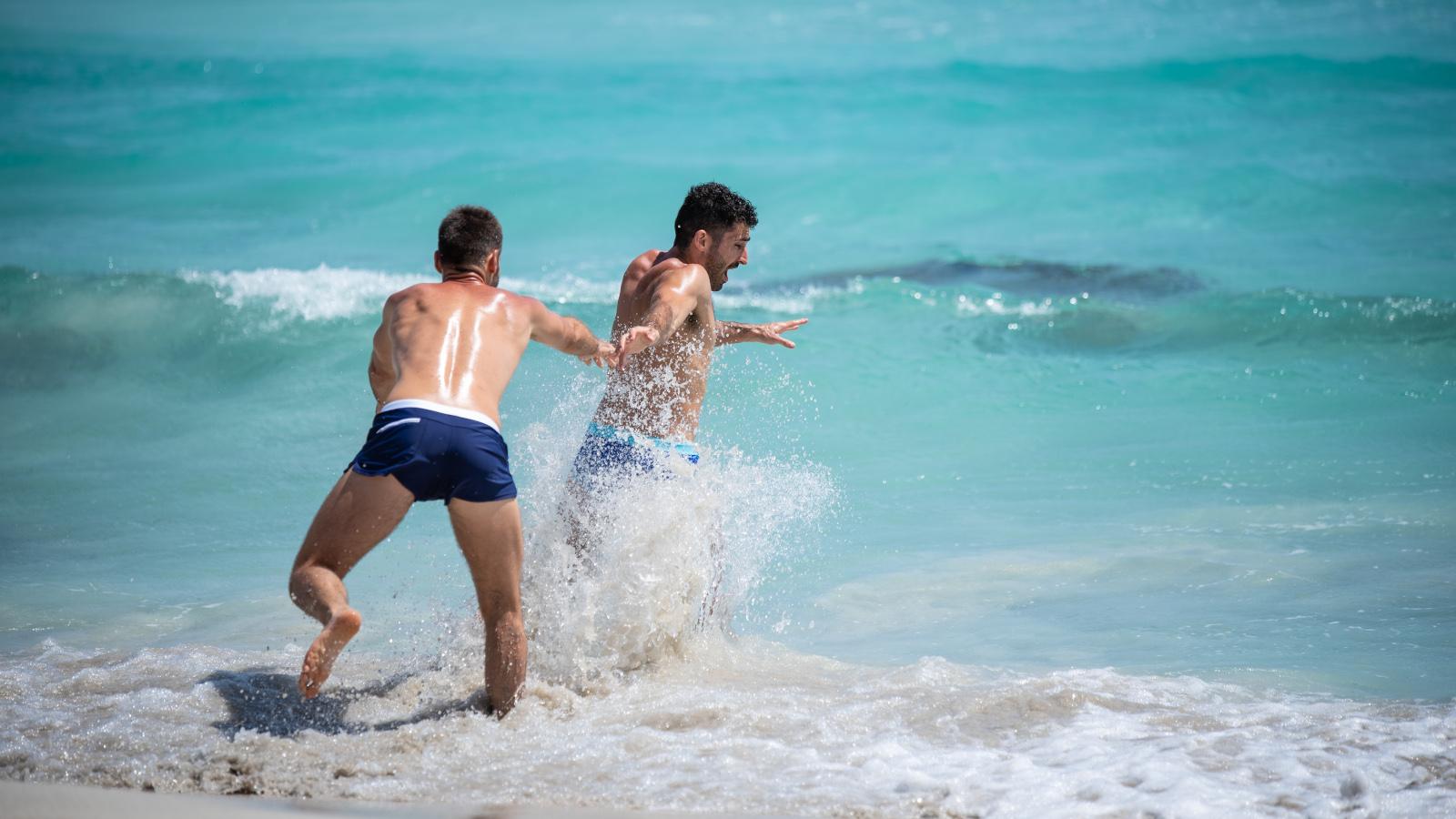 Nomadic Boys gay couple playing in the water at gay beach Nova Icaria in Barcelona