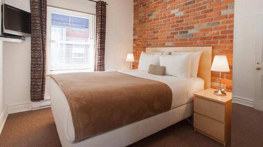 A cozy bedroom with a brick feature wall and tv at B&B Du Village BBV in Montreal.