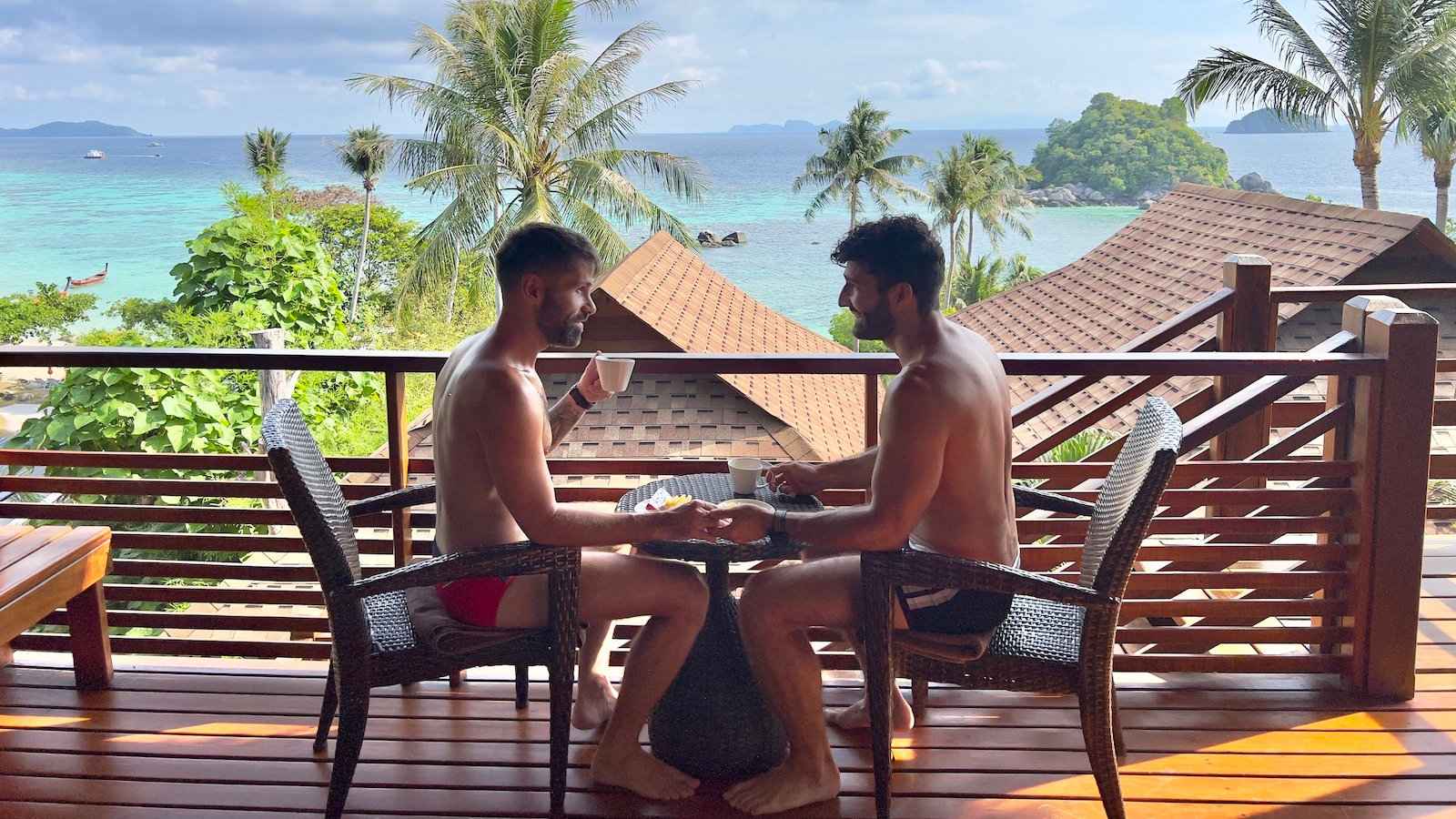 A gay couple enjoying breakfast on the deck at Ten Moons Resort with beach and palm tree views.