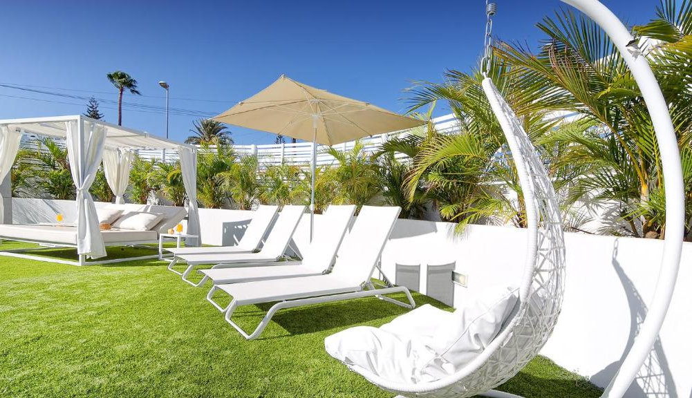 A series of white loungers, hanging chairs and sunbeds on a green lawn.