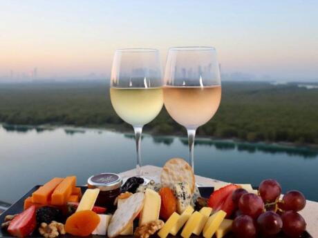 Two glasses of wine with a fruit and cheese platter in the foreground with the mangroves of Abu Dhabi in the background, as seen from high up in the Impressions rooftop bar!