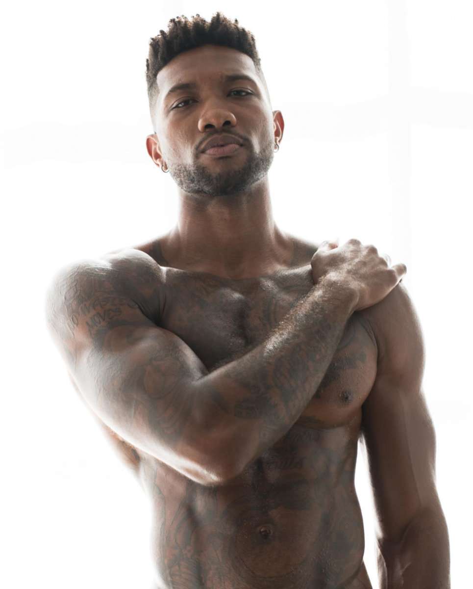 A fit tattooed black man staring at the camera with a white background.