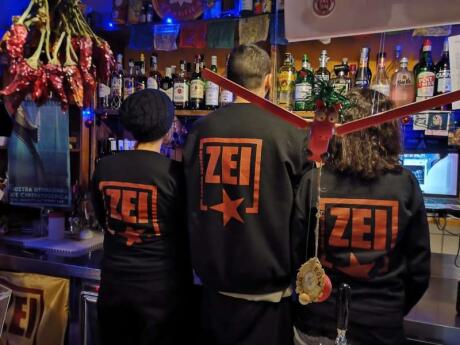 Staff at Zei Spazio Sociale gay bar in Lecce standing with their backs to the camera showing their sweaters with Zei on the back.