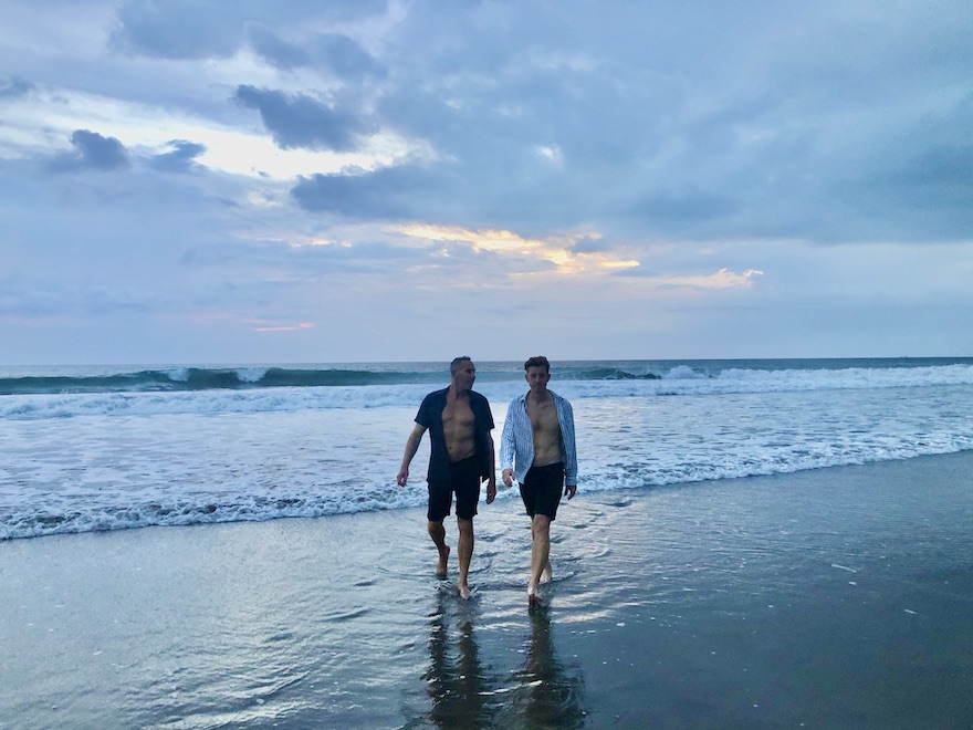 Gay couple walking on beach.