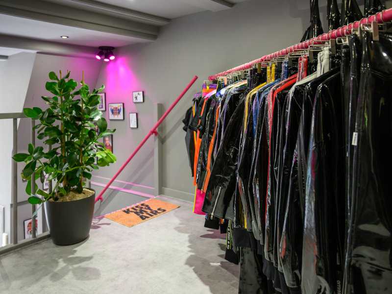 The interior of House of Riegillio in Amsterdam with black pvc clothing on hangers next to a potted plant.