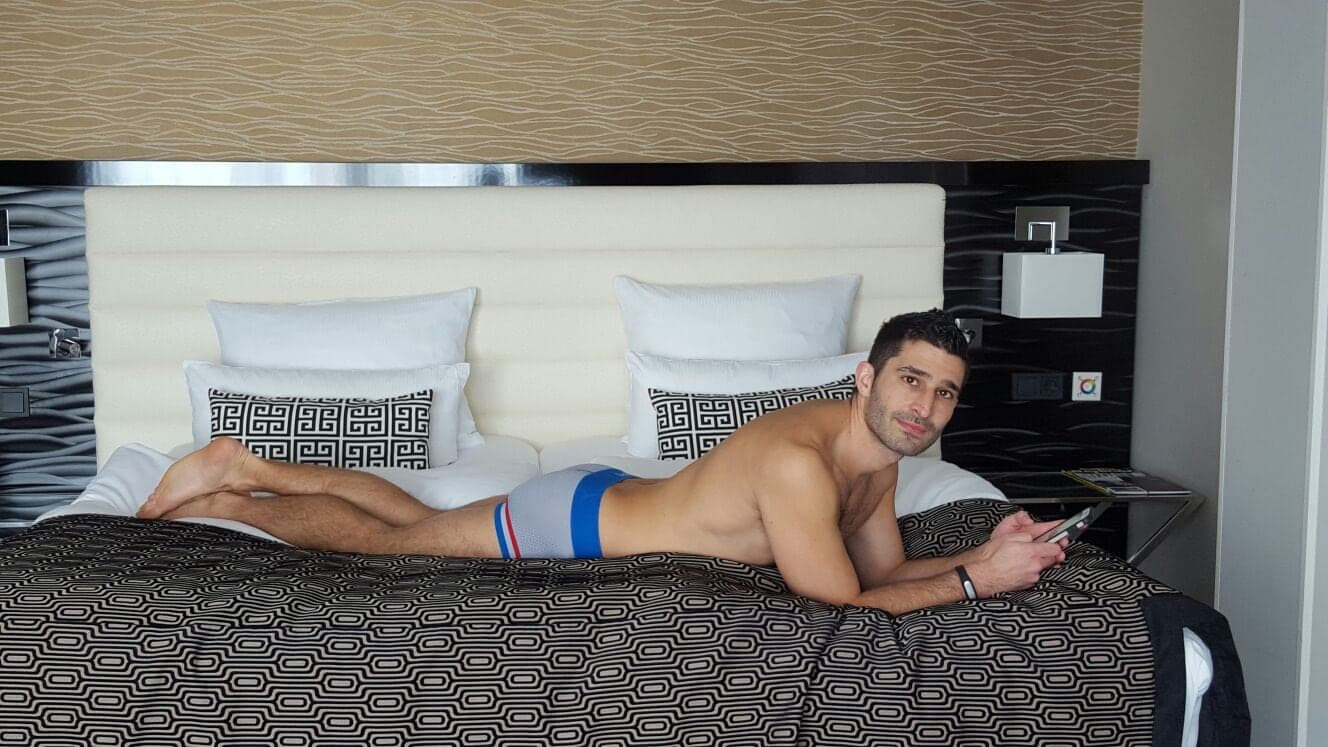Stefan in PUMP! gay underwear on a bed on his phone.