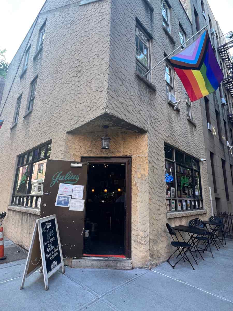 The grey exterior of Julius' gay bar in New York City, with a rainbow flag flying proud.