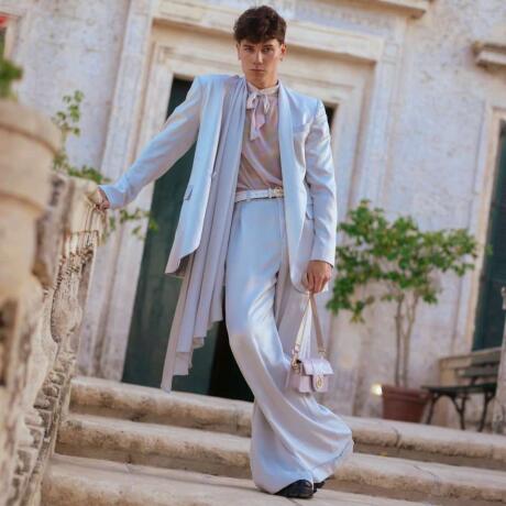 Nicky Champa, a gay Tik Tok influencer posing in front of a swanky villa in a beautiful silk suit.