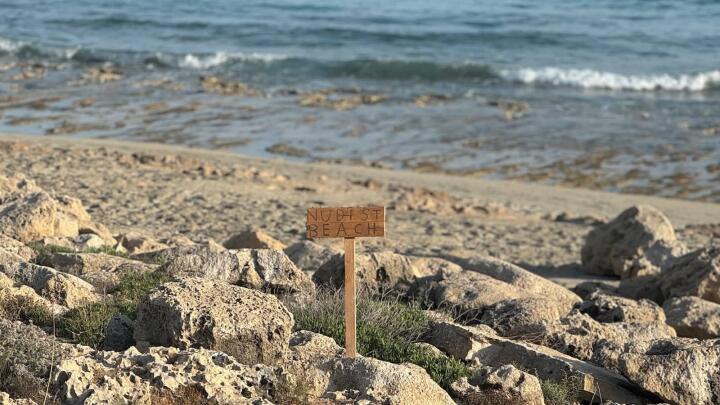 Agia Napa nudist beach sign on rocks by the sea.