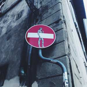 A stop sign in Florence with a sticker of Michelangelo's David appearing to hold the white bar in the red circle.