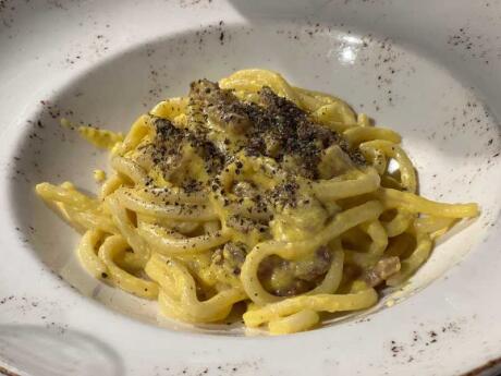 A close up shot of cheesy spaghetti pasta in a white bowl.
