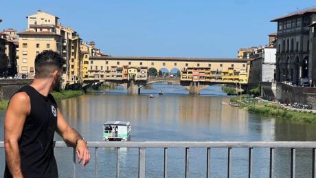 Stefan leaning on a bridge over a river looking back at the Ponte Vecchio bridge in Florence.