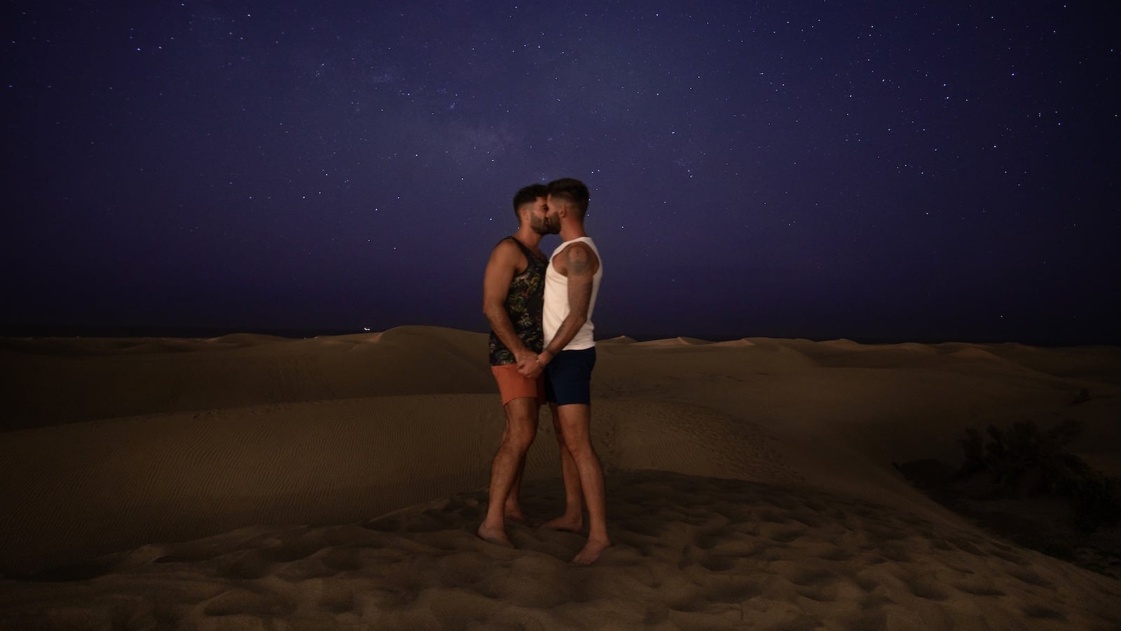 Gay couple kissing in the Maspalomas Sand Dunes under the starlight.