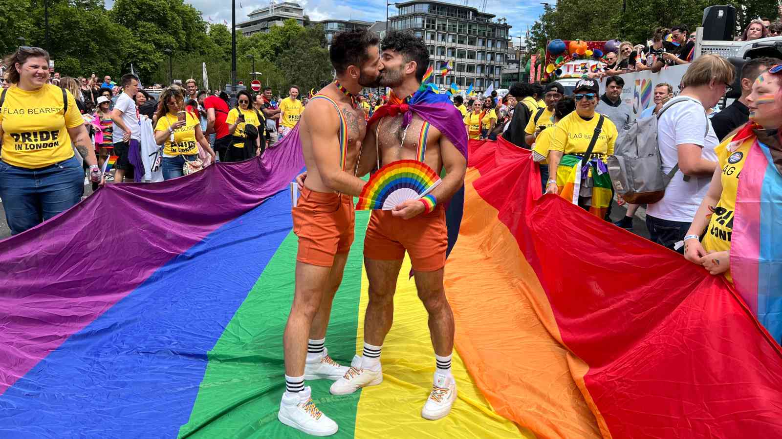 Gay couple kissing on rainbow flag at London Pride Parade.