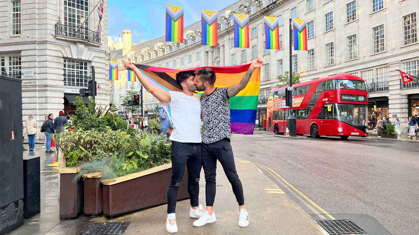 Gay couple kissing in Regent Street in London with the gay flag.