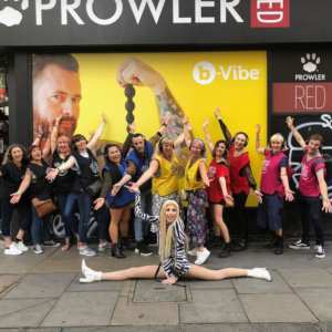 A tour group with a drag queen doing the splits in front, posing in front of Prowler shop in London, Soho.