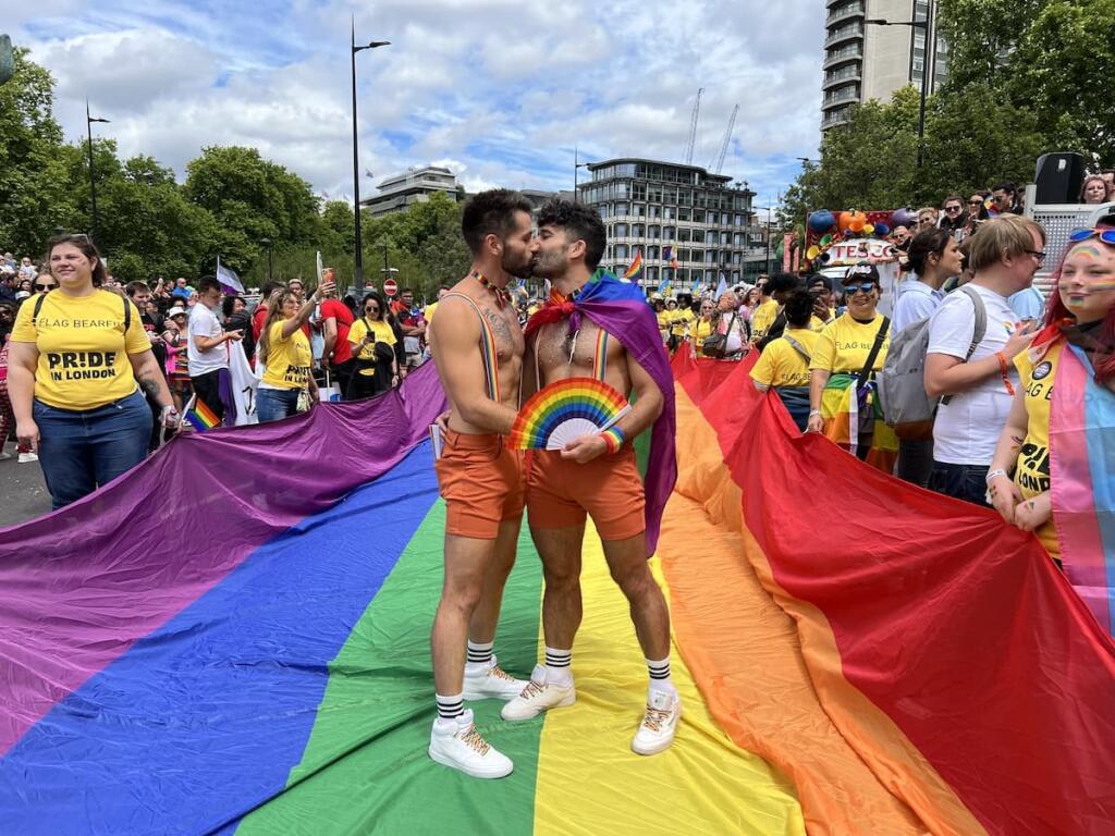 Gay couple kissing on rainbow flag at the London Pride Parade.