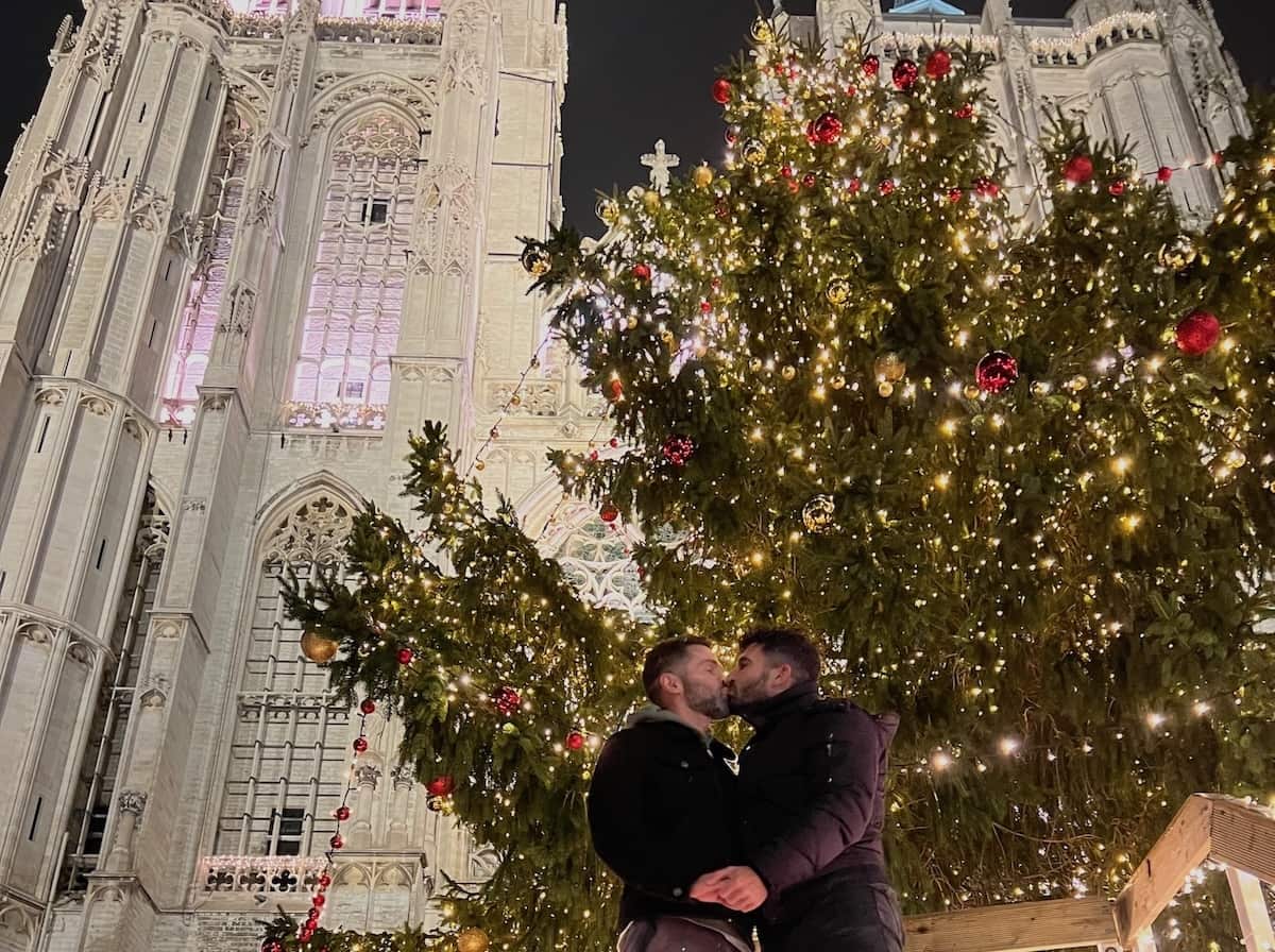Gay couple kissing in front of Christmas tree in Antwerp old town in Belgium.