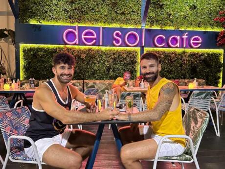 Seby and Stefan of Nomadic Boys holding hands at a table outside Del Sol Cafe in Athens.