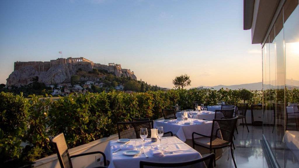 A sunset view of the rooftop restaurant at Electra Palace in Athens with a view of the Acropolis.