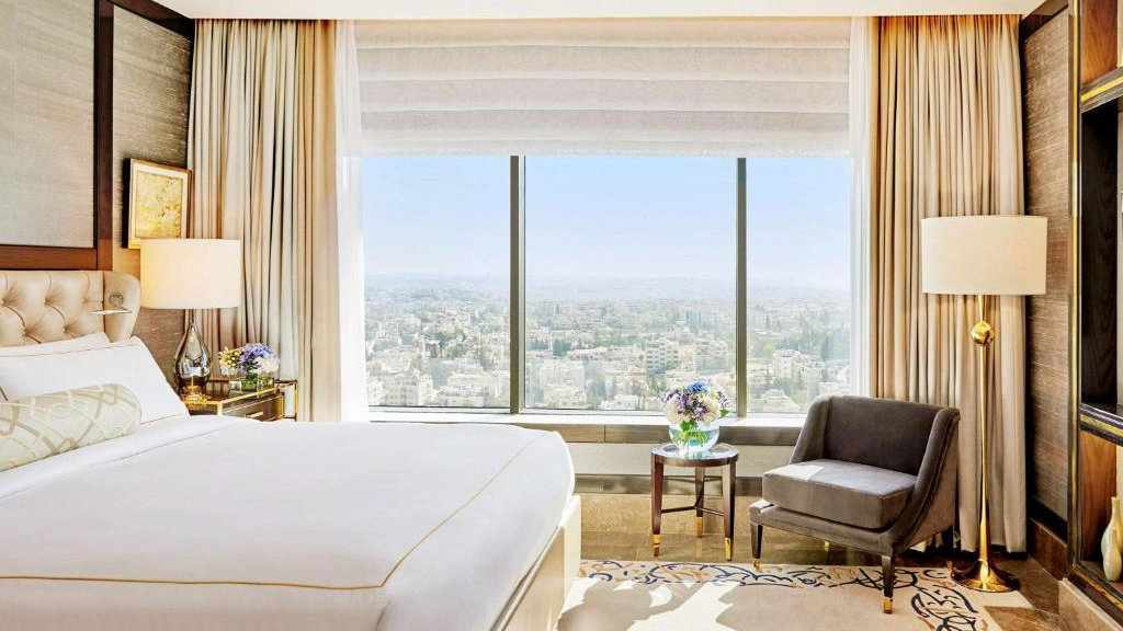 A light and airy hotel room with a high-up city view on a clear sunny day at the Fairmont in Amman.