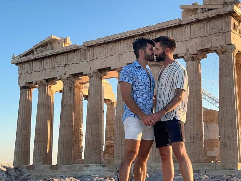 Stefan and Seby of Nomadic Boys sharing a kiss in front of the Acropolis in Athens.