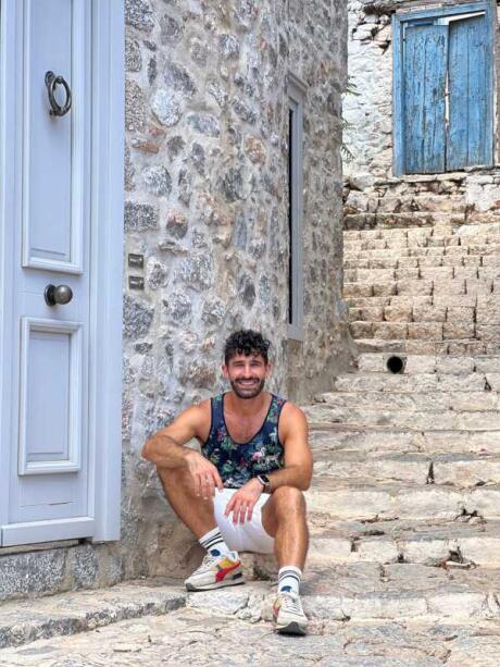 Stefan sitting on stony steps with old doors behind him on Hydra Island.