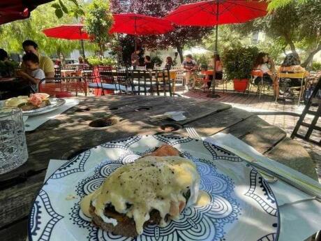A plate of eggs Benedict with tables and umbrellas in the garden at Klostirion cafe in Athens.