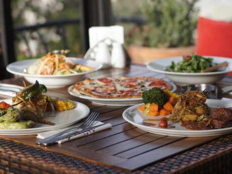 Plates of food including pizza on a table with plants behind from Mijana restaurant in Amman.