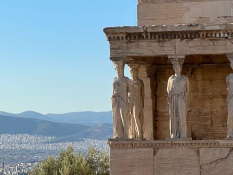 Blue skies over Athens with statues on the Porch of Caryatids at the Acropolis on the right side.