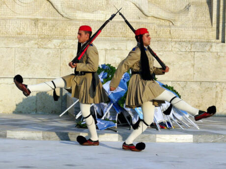 Two soldiers in uniform holding rifles marching in front of a wall during the Syntagma changing of the guards in Athens.