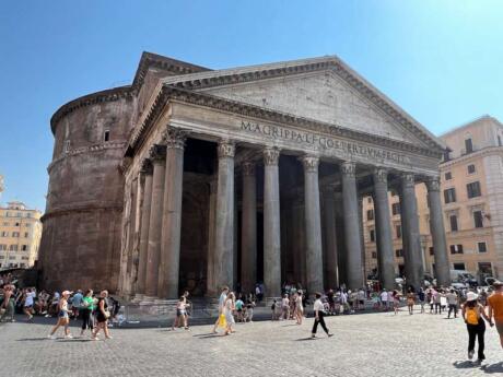 The massive Pantheon in Rome on a sunny day with small people wandering around in front.