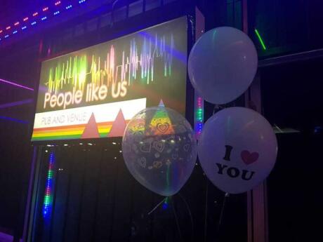 Balloons and fluro lights in a dark room with a screen showing People Like Us pub and venue.