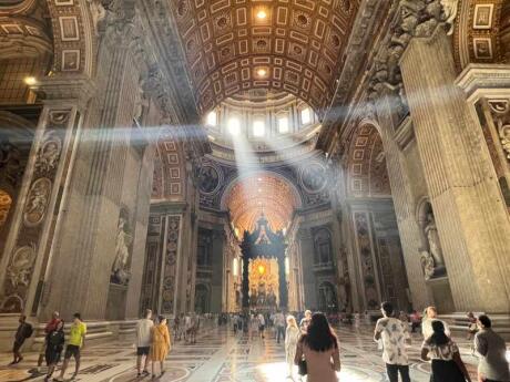 Light slanting down into the vast St Peter's Basilica in Vatican City with people wandering around.