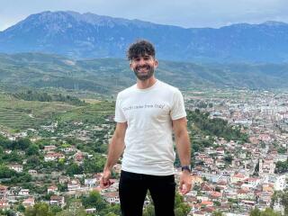 Stefan standing in front of a town and hills in the distance, wearing a white t-shirt that says 