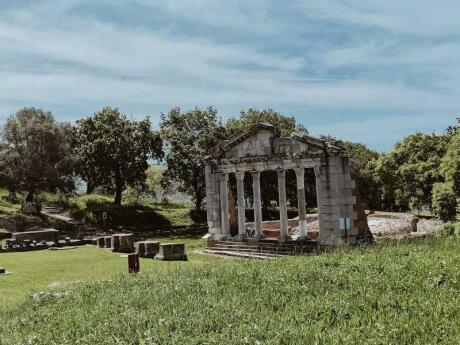 The ruins of an ancient Greek temple on green grass under a blue sky.