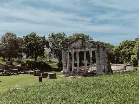 The ruins of an ancient Greek temple on green grass under a blue sky.