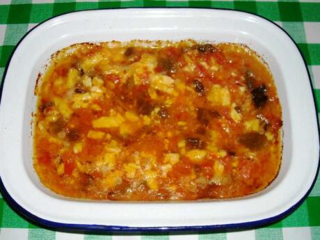 A white dish on a green checked cloth with a mix of tomatoes and vegetables in a red broth.