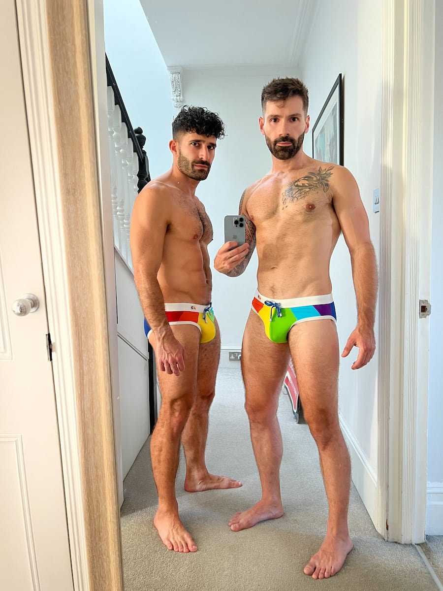 Stefan and Sebastien posing in a hallway in rainbow colored speedos and nothing else!