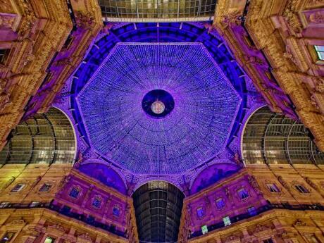 The ceiling of Galleria Vittorio Emanuele II in Milan lit up with purple Christmas lights at night.