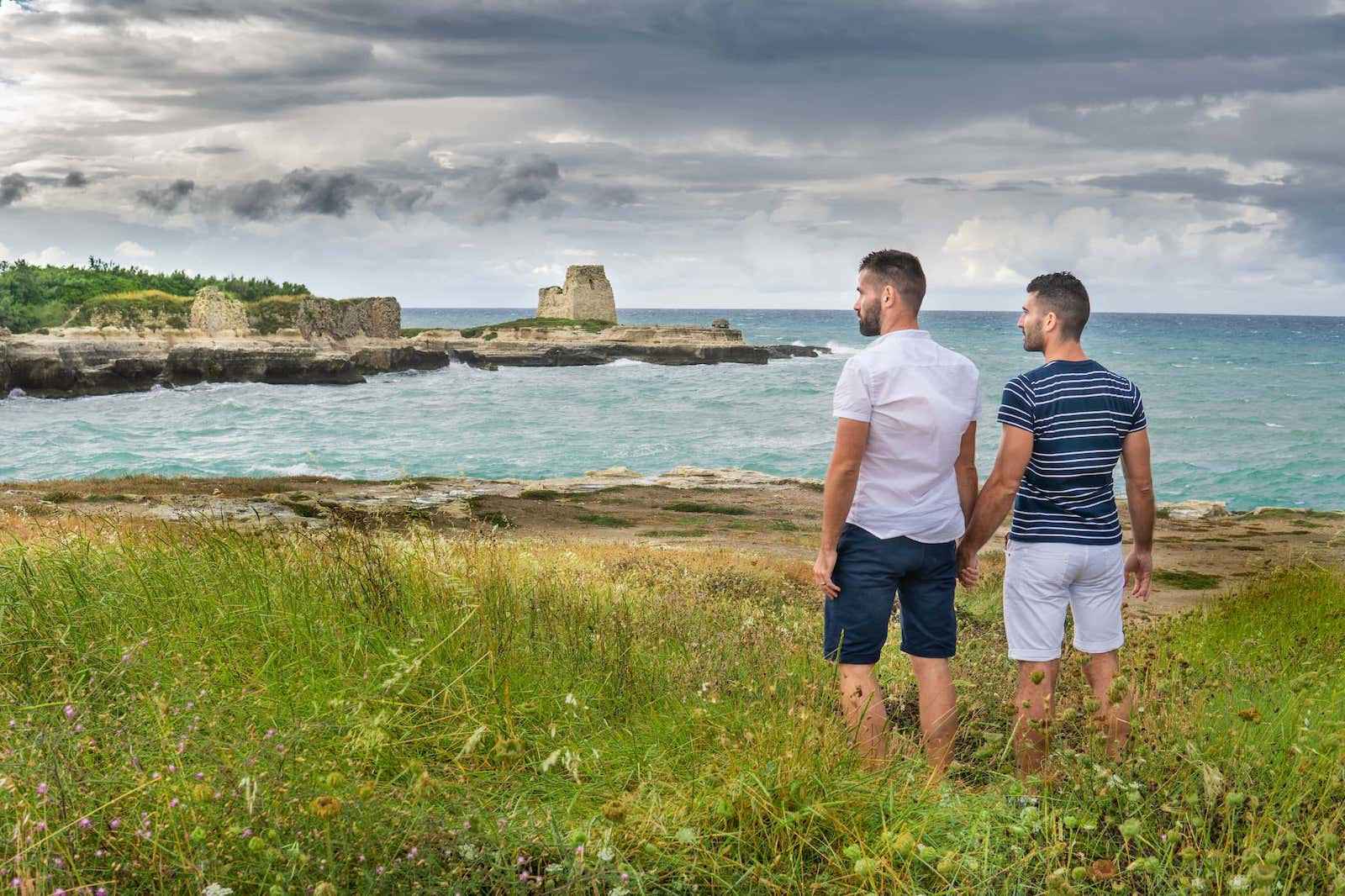 Nomadic Boys holding hands and standing on grass looking out over a headland with a stormy sky in Puglia in italy.