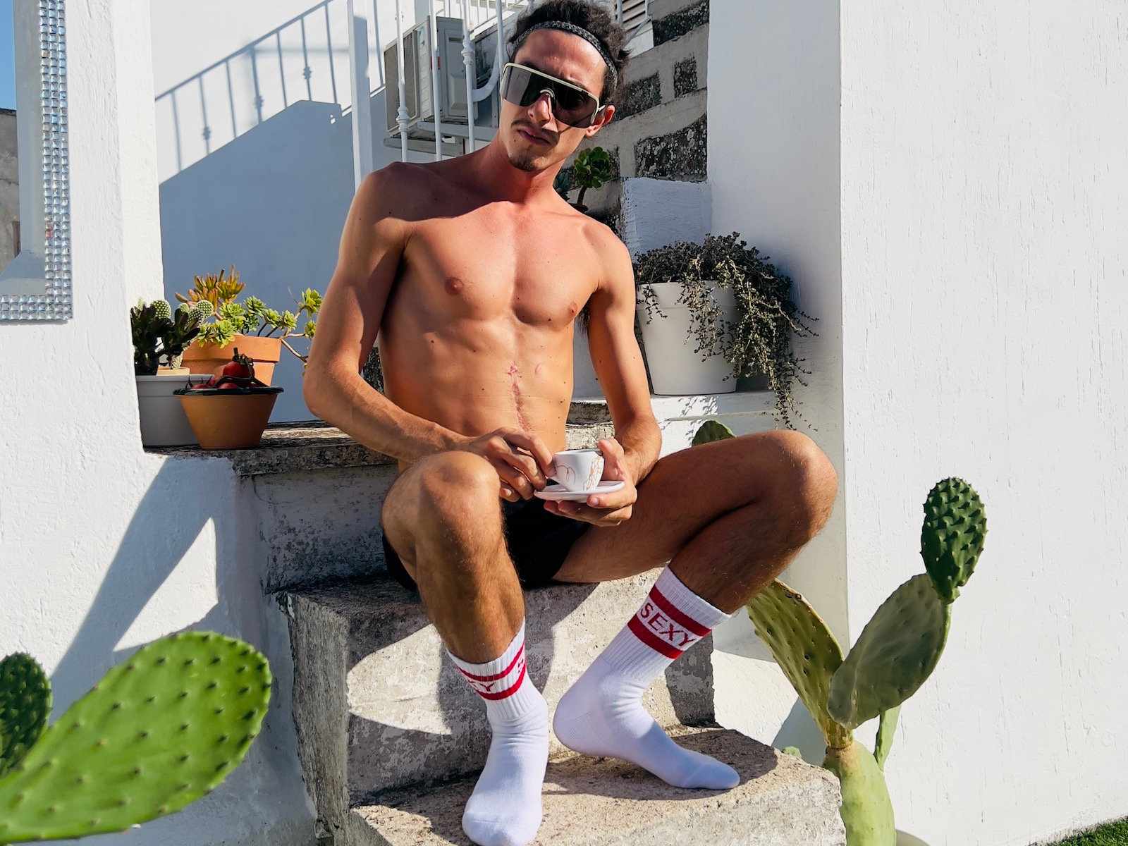 Gay hot guy in underwear and socks that say "sexy" sitting on some steps having coffee.