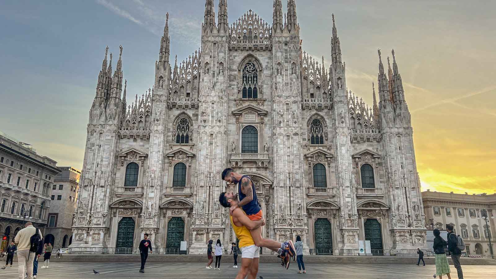 A gay couple with one man lifting the other up in front of the Milan Cathedral.