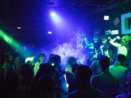 Large crowd of gay men dancing at the Q Club in Milan under blue and green lights and smoke.