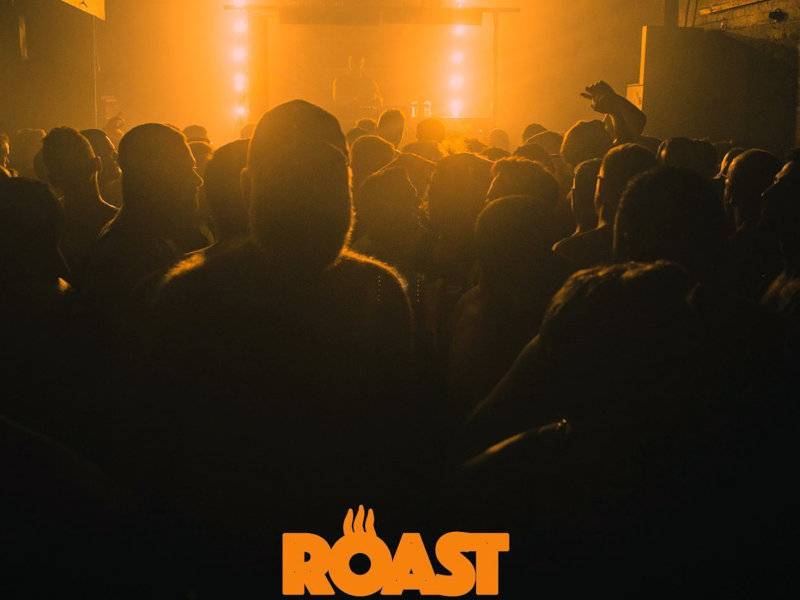A hazy photo of men dancing at a club with orange lighting and the word Roast.