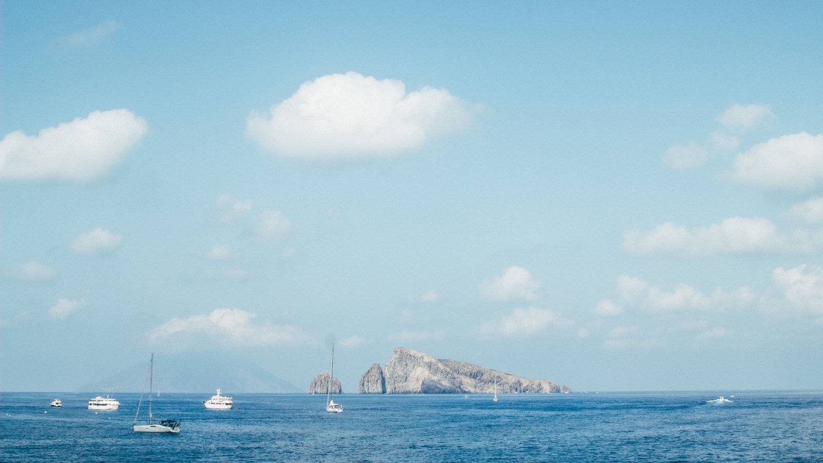 A view of yachts and a rocky outcrop on a beautiful clear day.