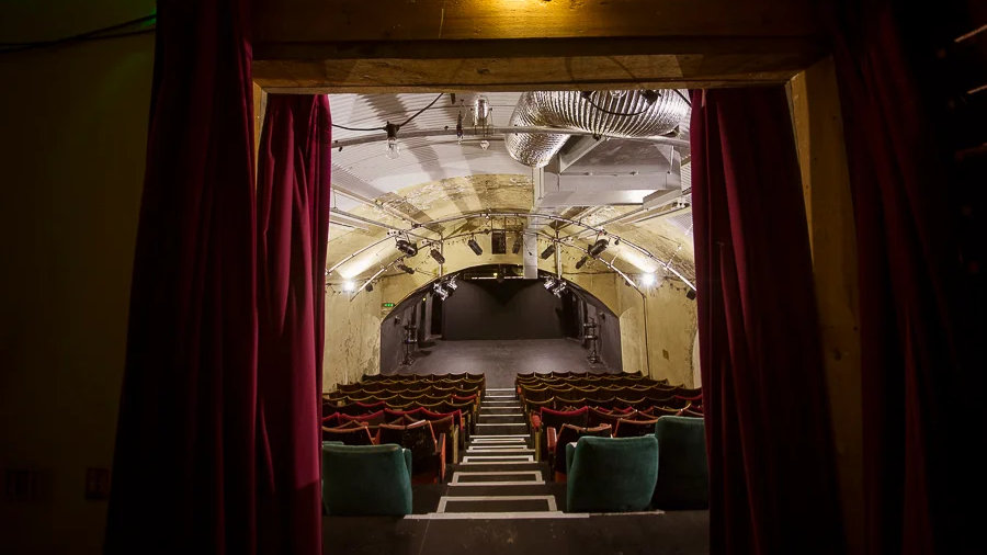 The interior entrance view of the Vaults Theatre in London, framed by red curtains.
