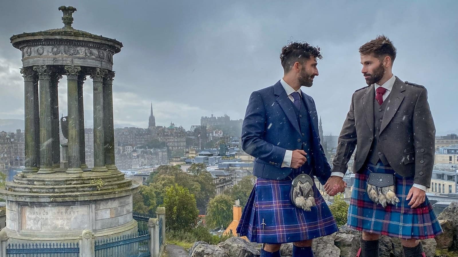 Gay couple in kilts holding hands at Carlton Hill in Edinburgh, Scotland.